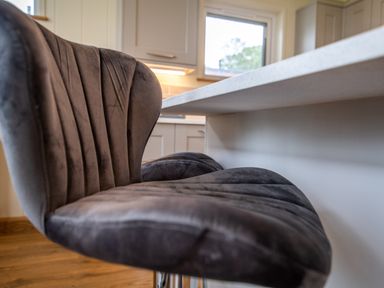 A close up of a grey cushioned bar stool by a white kitchen counter at Otter Lodge in Gargrave