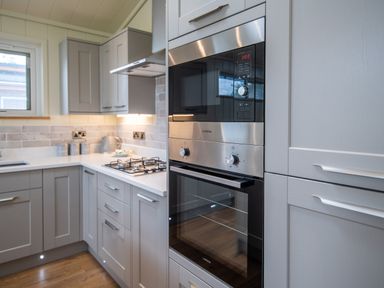 A kitchen with grey cabinets a gas stove a microwave and an oven at Otter Lodge in Gargrave