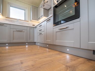 A kitchen with grey cabinets wooden floor and under cabinet lighting at Otter Lodge in Gargrave