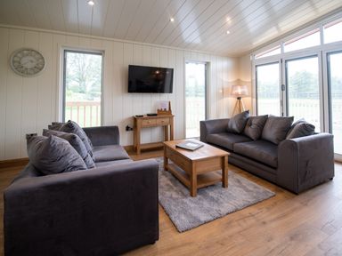 A living room with two sofas a wooden coffee table a wall clock and a television at Otter Lodge in Gargrave
