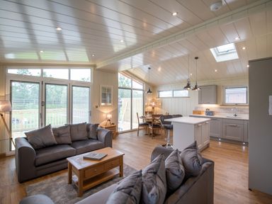 An open living room and kitchen area with sofas a coffee table dining table and kitchen island at Otter Lodge in Gargrave