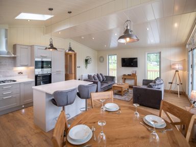 An open living room and kitchen with a wooden dining table set with plates and glasses at Otter Lodge in Gargrave