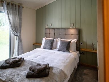 A bedroom with a bed with pillows and towels near a window with curtains at Otter Lodge in Gargrave