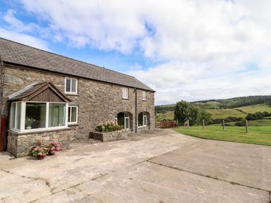 An exterior view of a stone building with windows and flower pots next to a concrete driveway and green fields at The Stables At Cae Gwyn in Ruthin