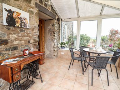 A conservatory with a round table and four chairs a vintage sewing machine table and plants by the windows at The Stables At Cae Gwyn in Ruthin