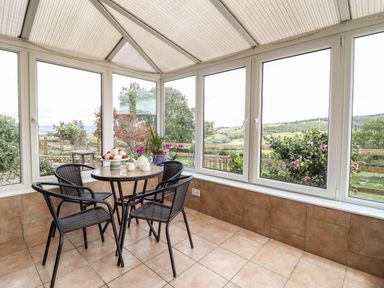 A conservatory with a round table and four chairs overlooking a garden at The Stables At Cae Gwyn in Ruthin
