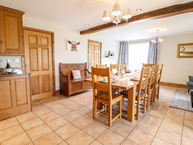 A dining room with a wooden table set with chairs and a wooden bench against the wall at The Stables At Cae Gwyn in Ruthin