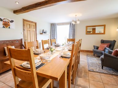 A dining room with a wooden table set for eight and two armchairs on a rug at The Stables At Cae Gwyn in Ruthin