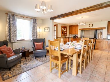 A dining area with a wooden table set for meals and two armchairs with cushions near a window at The Stables At Cae Gwyn in Ruthin