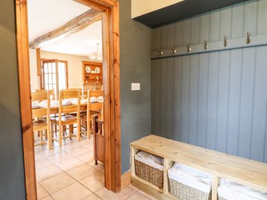 A hallway with wooden bench and coat hooks looking into a dining room with wooden chairs and table at The Stables At Cae Gwyn in Ruthin