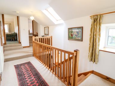 A hallway with carpeted floors wooden railing a window with curtains and framed artwork at The Stables At Cae Gwyn in Ruthin
