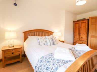 A bedroom with a wooden bed frame two bedside tables with lamps and a wooden wardrobe at The Stables At Cae Gwyn in Ruthin