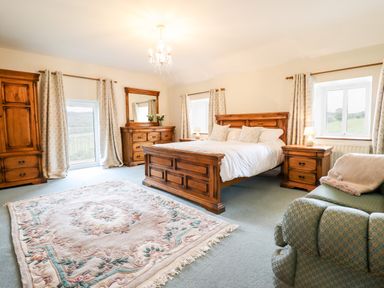 A bedroom with a wooden bed frame a dresser a wardrobe two nightstands an armchair and a rug at The Stables At Cae Gwyn in Ruthin