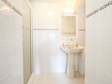 A bathroom with a pedestal sink a mirror above and a shower with a frosted glass door at The Stables At Cae Gwyn in Ruthin