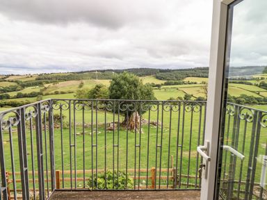 A view from a balcony with metal railing overlooking green fields trees and hills at The Stables At Cae Gwyn in Ruthin