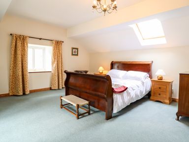 A bedroom with a wooden bed bedside tables and a window with curtains at The Stables At Cae Gwyn in Ruthin