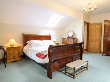 A bedroom with a wooden bed, nightstands with lamps, dresser with mirror, wardrobe, and a small bench at The Stables At Cae Gwyn in Ruthin