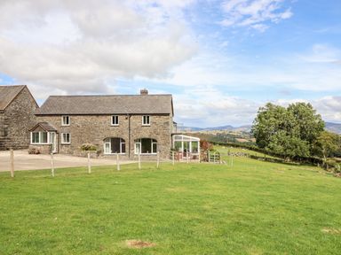 Stone house with a green lawn and trees in the countryside at The Stables At Cae Gwyn in Ruthin