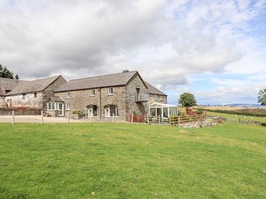 A stone farmhouse with an attached barn and glass conservatory on a grassy field at The Stables At Cae Gwyn in Ruthin
