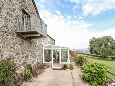 An outdoor area with a stone building balcony and a glass conservatory overlooking a garden and countryside at The Stables At Cae Gwyn in Ruthin