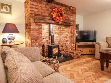 A living room with brick fireplace wood stove beige sofas television and wooden furniture at The Stables At Cae Gwyn in Ruthin