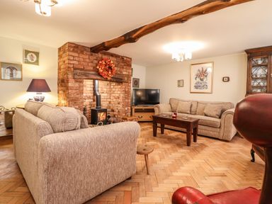 A living room with two beige sofas a brick fireplace with a wood stove a wooden coffee table and a television at The Stables At Cae Gwyn in Ruthin