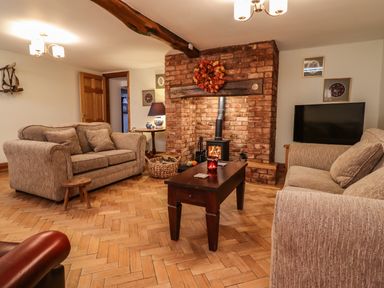 A living room with two beige sofas a coffee table a brick fireplace and a television at The Stables At Cae Gwyn in Ruthin