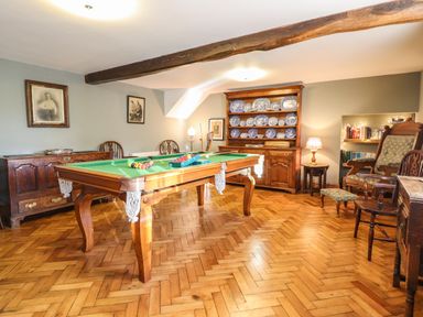 A room with a pool table a wooden cabinet with blue and white plates chairs and wooden flooring at The Stables At Cae Gwyn in Ruthin