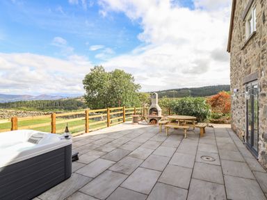 An outdoor patio area with hot tub picnic table and outdoor fireplace at The Stables At Cae Gwyn in Ruthin