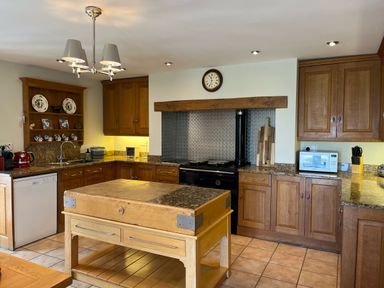 A kitchen with wooden cabinets a central wooden island a dishwasher a stove a microwave and shelving with plates at The Stables At Cae Gwyn in Ruthin