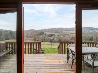 A wooden deck with outdoor furniture and a view of fields and hills at The Willow Lodge near Lyme Regis