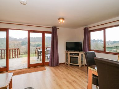 A living room with wooden floor dining table leather chairs and TV on wooden cabinet at The Willow Lodge near Lyme Regis