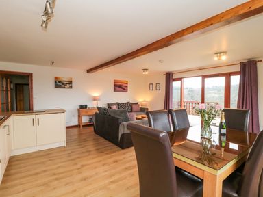 An open plan living and dining area with a wooden floor a dining table with chairs and flowers a sofa and large windows at The Willow Lodge near Lyme Regis