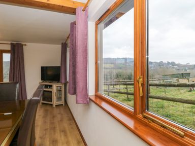 A dining area with brown chairs and curtains next to a window showing a fenced grassy field at The Willow Lodge near Lyme Regis