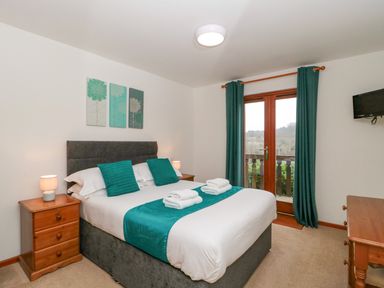 A bedroom with a double bed two bedside tables lamps and a balcony door at The Willow Lodge near Lyme Regis