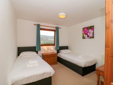 A bedroom with two single beds separated by a wooden nightstand with lamps and a window with green curtains at The Willow Lodge near Lyme Regis