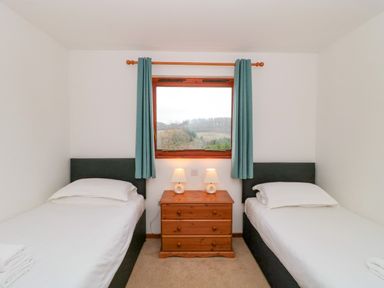 A bedroom with two single beds separated by a wooden nightstand with two table lamps and a window with curtains at The Willow Lodge near Lyme Regis