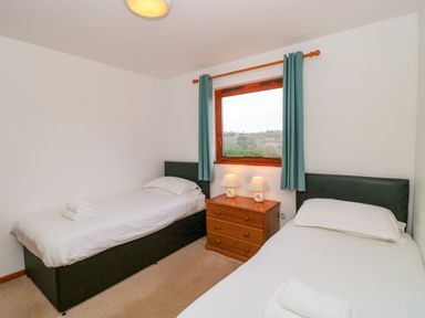 A bedroom with two single beds a wooden chest of drawers and a window with blue curtains at The Willow Lodge near Lyme Regis