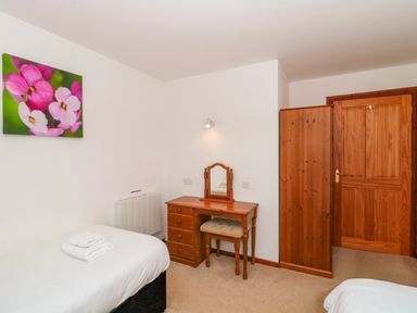 A bedroom with two single beds a wooden dressing table a chair a wooden wardrobe and a painting of pink flowers on the wall at The Willow Lodge near Lyme Regis