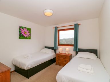 A bedroom with two single beds a wooden chest of drawers and a window with curtains at The Willow Lodge near Lyme Regis