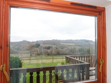 A window with wooden frame overlooking a balcony garden and a landscape of trees and hills at The Willow Lodge near Lyme Regis