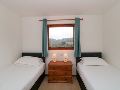 A bedroom with two single beds and a wooden dresser with lamps under a window with blue curtains at The Willow Lodge near Lyme Regis