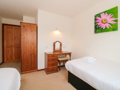 A bedroom with two single beds a wooden wardrobe a wooden dressing table with mirror and a pink flower picture on the wall at The Willow Lodge near Lyme Regis