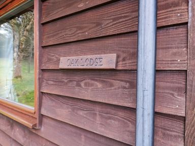 A wooden exterior wall with a small sign reading oak lodge and a window showing trees outside at The Oak Lodge near Lyme Regis