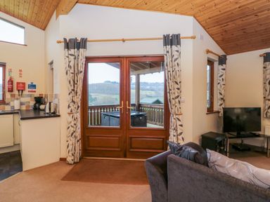 A living room with a sofa a television and glass doors leading to a balcony at The Oak Lodge near Lyme Regis