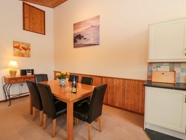 A dining room with a wooden table and six black chairs a side table with a lamp and radio and kitchen cabinets with a bread box at The Oak Lodge near Lyme Regis