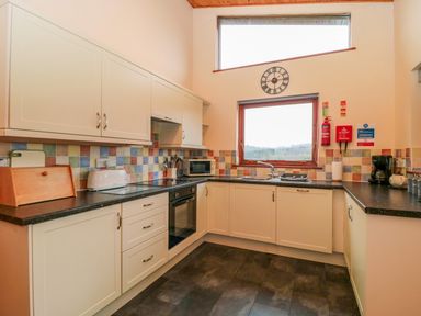 A kitchen with cream cabinets dark countertops multicolored tile backsplash a window a clock toaster oven and coffee maker at The Oak Lodge near Lyme Regis