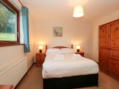 A bedroom with a double bed two bedside tables with lamps a wooden wardrobe and a window at The Oak Lodge near Lyme Regis
