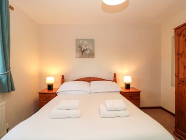 A bedroom with a double bed two bedside tables with lamps a wooden wardrobe and a painting above the bed at The Oak Lodge near Lyme Regis