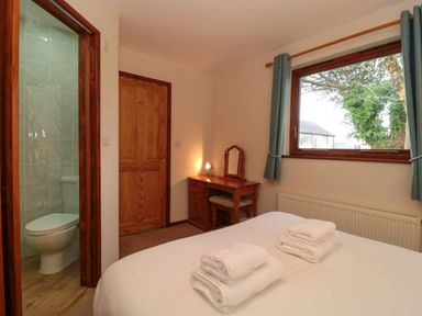A bedroom with a bed with towels on it a wooden dressing table a window and a bathroom visible at The Oak Lodge near Lyme Regis